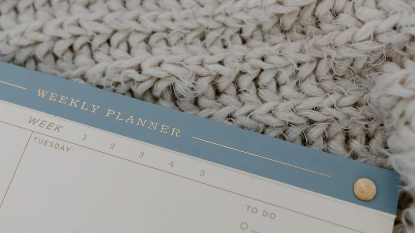 A weekly planner labelled by day resting on a soft knitted blanket.