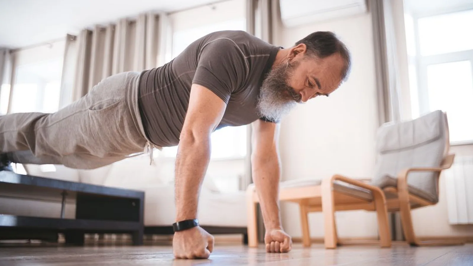 A man doing a push-up on the floor of his living room in the morning light.