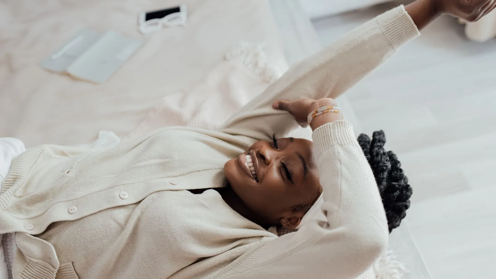 A smiling woman stretching in bed in the morning light, her phone lying unused beside her.
