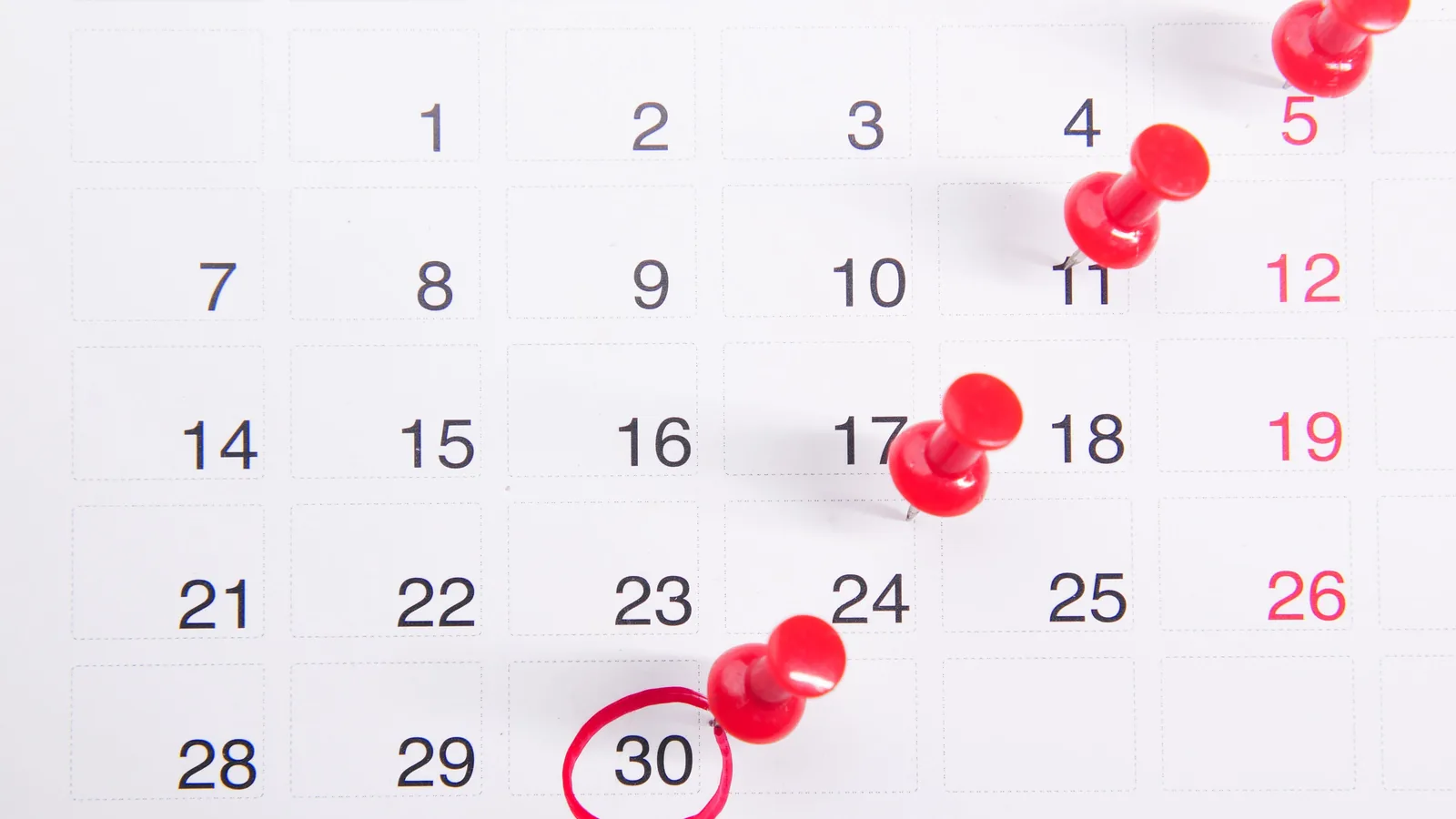 Close-up of a calendar with red push pins marking important dates, emphasizing deadlines.