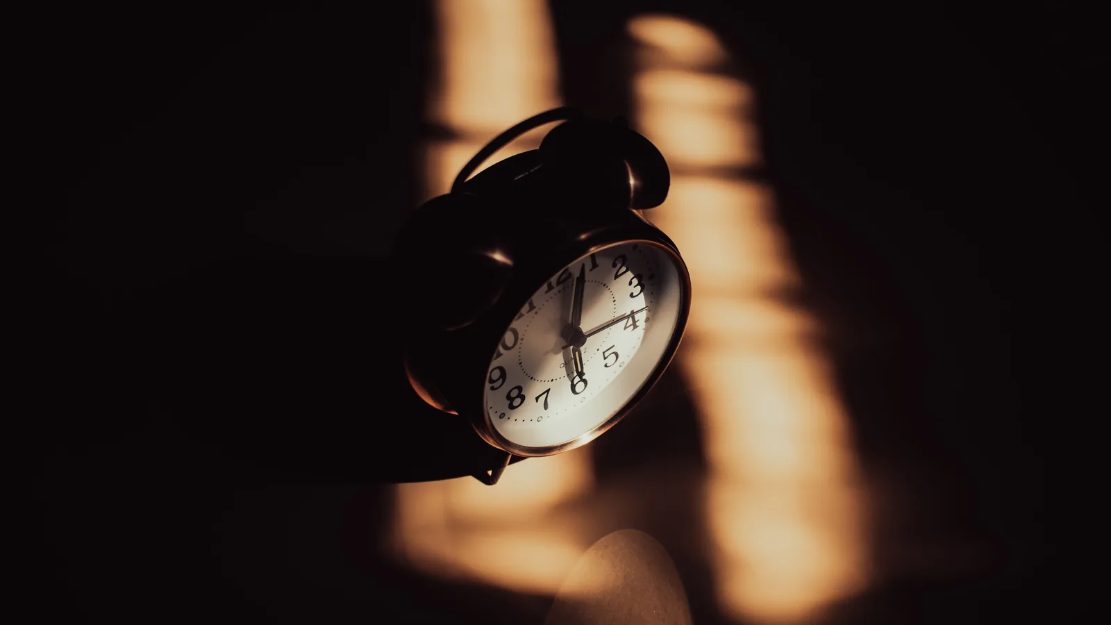 A retro analog alarm clock in moody shadows and warm lighting.