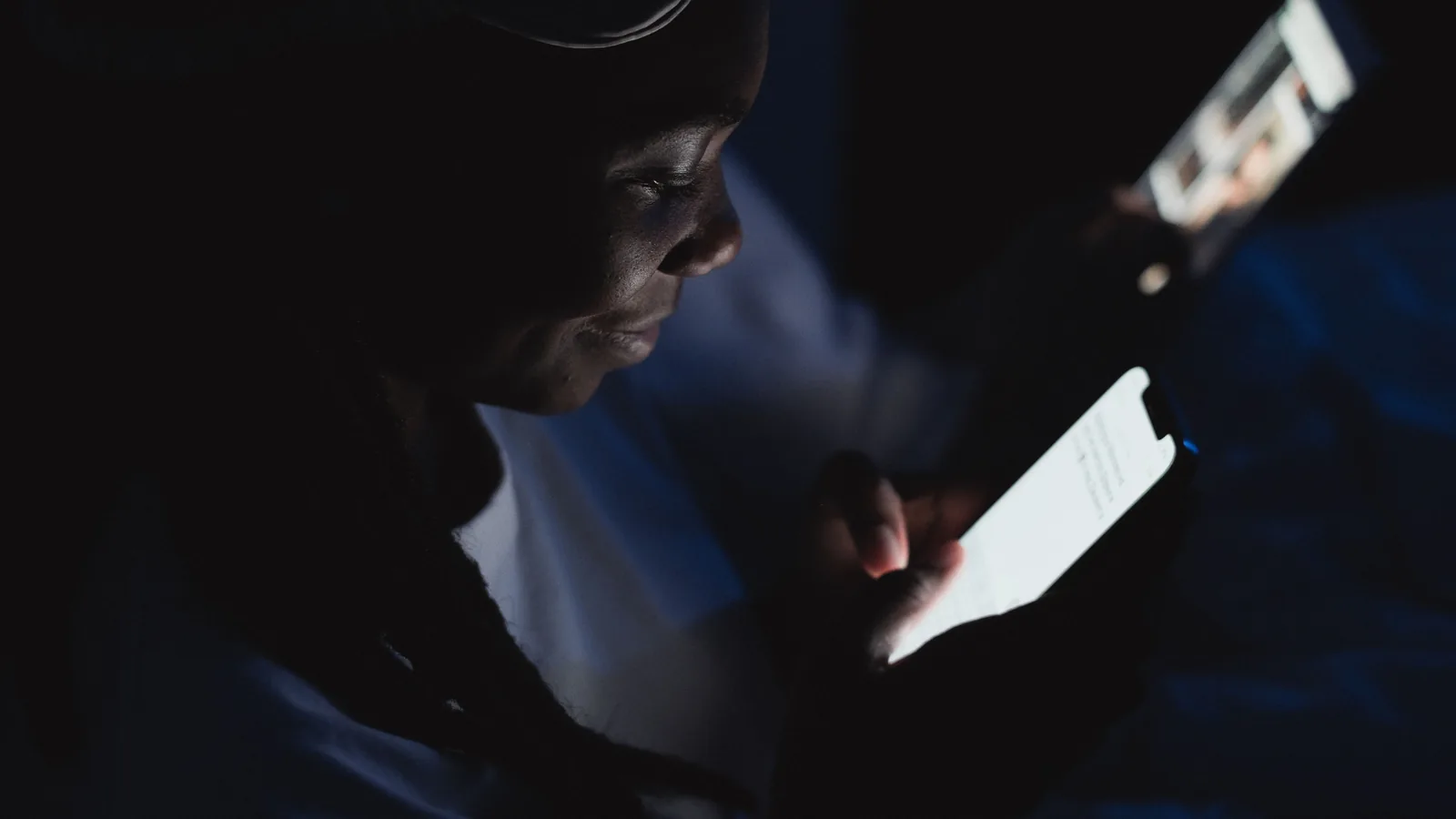 Close-up of a woman reading on her smartphone in a dark room, illuminated by the screen.